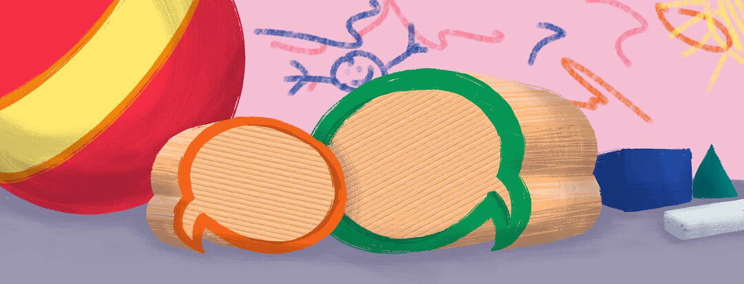 Children's blocks shaped like speech bubbles sit on a table in front of a wall drawn all over with crayon